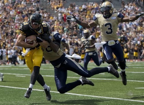 Hamilton Tiger-Cats Dan LeFevour scores a touchdown past Winnipeg Blue Bombers Alex Hall (C) and Cauchy Muamba (R) during the first half of their CFL football game in Guelph, August 24, 2013.  REUTERS/Mark Blinch (CANADA - Tags: SPORT FOOTBALL) - RTX12VAR