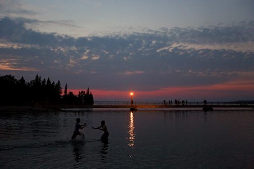 Brandon Sun 24082013 Kids play in the water of Clear Lake while people stroll along the pier after sunset on a muggy Saturday evening.  (Tim Smith/Brandon Sun)