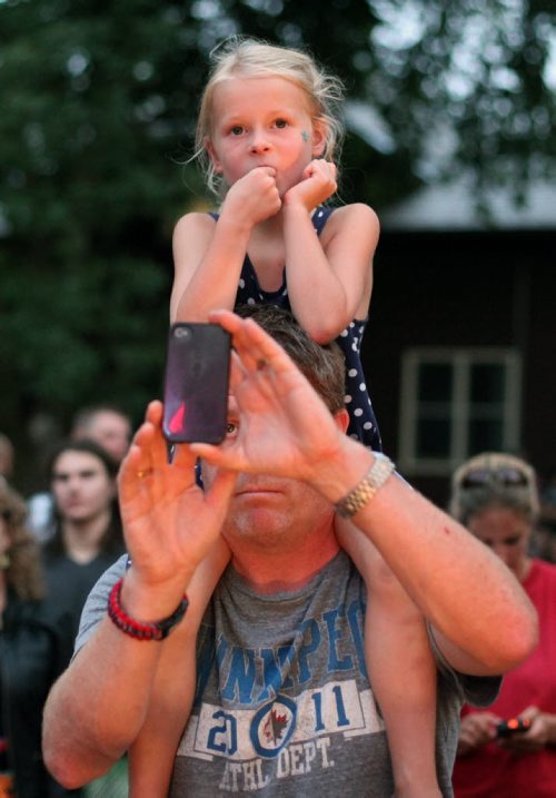 Brandon Sun 24082013 A fan takes a photograph with a young girl on his shoulders as Glass Tiger performs during a free concert in honour of Riding Mountain National Park's 80th Anniversary on Saturday evening. Fans filled the grass and the beach adjacent to Clear Lake for the concert which also included performer Jess Moskaluke. (Tim Smith/Brandon Sun)
