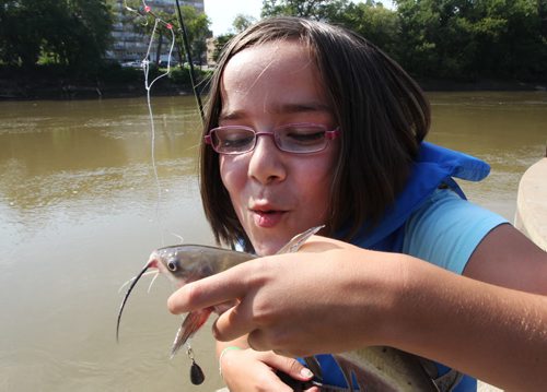 11 year old Tiana Lagan from the Tuxedo Family Resource Center pretends to kiss a small channel cat she caught on the Assiniboine River Tuesday- She with her classmates were fishing today to celebrate the success of the Winnipeg Youth-at-Risk Program that saw over 400 Winnipeg youth enjoy a day of fishing--Standup Photo - August 27, 2013   (JOE BRYKSA / WINNIPEG FREE PRESS)