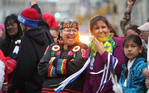Jingle dancers Jacqueline Daniels (left)  and her friend Naomi  Fosseneuve share some laughs as they gather together with a large group of  drummers and jingle dancers  at the corner of Portage and Main welcoming the UN Special Rapporteur on the Rights of Indigenous Peoples Saturday morning.  The dance was followed by a march down to Thunderbird House.  Oct   12,, 2013 Ruth Bonneville Winnipeg Free Press