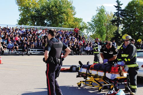 Canstar Community News Students from Oak Park High School and Gray's Academy observe a mock car crash and the aftermath Wednesday morning. The mock collision was put on by the Manitoba Brain Injury Association to educate young drivers about the risks of distracted or impaired driving and the effects it can have on friends, family and first responders.