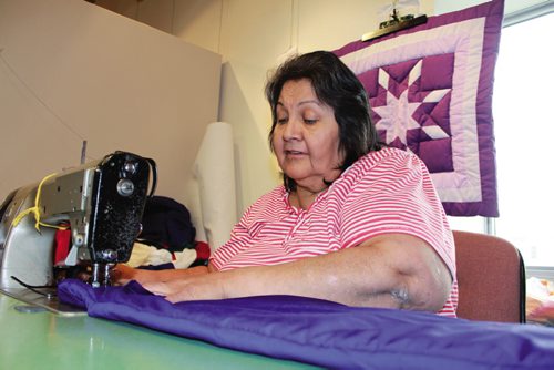 Canstar Community News Viola sews together another Star Blanket at Neechi Commons, with a finished blanket hanging in the background. (JORDAN THOMPSON)  NOTE: Did not want her last name published.