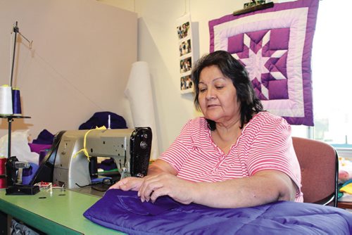 Canstar Community News Viola sews together another Star Blanket at Neechi Commons, with a finished blanket hanging in the background. (JORDAN THOMPSON)  NOTE: Did not want her last name published.