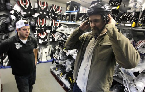 Spartan Sports employee Mike Ducharme, left, with Marcus Malbasa trying on a hockey helmet. The story is about the Jets banning helmets to Chicago game tomorrow night to mock what that drunk guy did to Pardy in Chicago a few weeks ago. Marcus is a Jets fan who doesnt agree with the decision.. BORIS MINKEVICH / WINNIPEG FREE PRESS  November 20, 2013