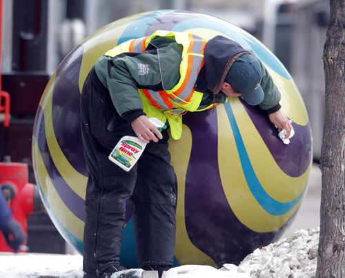 Downtown Biz employee David Messenger cleans and polishes spheres on Portage Ave. near the MTS Centre. from the web: There are sixteen 3 marbles and five 46 diameter marbles along Portage. The marbles are made out of six different colours of gel coat resin that is sprayed into two separate mould halves. The two pieces are then glued together forming the sphere. The ball is then sanded to get rid of any imperfections and the seam finished/smoothed over with bondo. The designs were then taped out and painted onto the marbles with automotive paint. The glowing lights are achieved from the natural gel coat colour that is covered with two to three layers of top coat. A 100 Watt bulb is placed inside the marble to create the glowing effect. They were installed by groundhog anchors. The plants are planted in a felt pocket inside the marble. The Marbles on Portage project was officially opened at noon on July 31, 2012 with ice cream and marble give-aways in Air Canada Park. BORIS MINKEVICH / WINNIPEG FREE PRESS  December 2, 2013