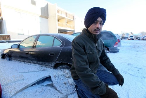 Amandeep Sidhu crouches  next to his vehicle that froze to the ground when a  water main broke in the parking lot next to his apartment on New Years Eve Day on Jefferson. Jan 02, 2014 Ruth Bonneville / Winnipeg Free Press