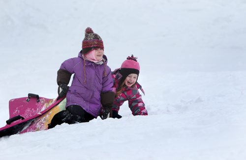 Five year old Emily Aikman (right)  giggles  as she pushes her sled up Omands Creek hill with her friend  Mya Tottle , also five, Saturday morning while enjoying the warm winter weather with their families. Standup photo  Jan 11,, 2014 Ruth Bonneville / Winnipeg Free Press