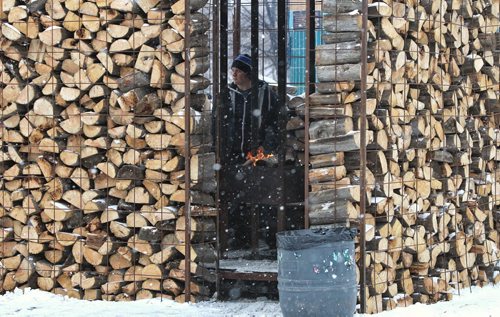 A visitor to The Forks warms up by a fire barrel inside a hut built of firewood Sunday afternoon.   140119 - January 19, 2014 MIKE DEAL / WINNIPEG FREE PRESS