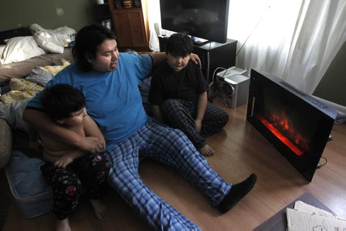 Derek Dowan and his two sons Dave,6 at left, and Daniel,9, keep toasty warm by the electric heater and heat from the kitchen stove in their home with out natural gas in Niverville Mb.Monday morning. It was 4C when the family woke up sleeping after sleeping in the living room. Adam Wazny story Wayne Glowacki / Winnipeg Free Press Jan.27 2014