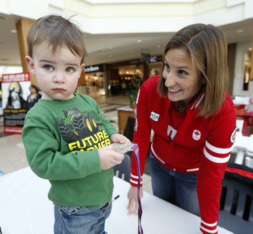Stdup Local Olympics  /  Wpg Olympian  Janine Hanson  winner of a silver medal  in women's eight's  rowing 2012  Summer Games in London  showing her silver medal to two and a half year old  Dylan Friesen   was on hand at a Polo Park opening of the Red Leaf Lounge at Centre Court , a big screen tv  and stage will be  on hand for customers to watch the Olympics in Sochi Russia  while shopping- 1988 Para Olympian Shep Shell , blind marathon runner was also  on hand tp meet the public on this the opening of the 2014 Olympics , FEB. 7 2014 / KEN GIGLIOTTI / WINNIPEG FREE PRESS
