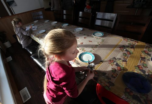 8 yr old Lisa works her way around the 18 ft long kitchen table setting forks. (and her sister Helen doing homework behind her). See Bill Redecopp story AND Video re: 13 orphaned kids adopted by their Uncle and Aunt. February 20, 2014 - (Phil Hossack / Winnipeg Free Press)