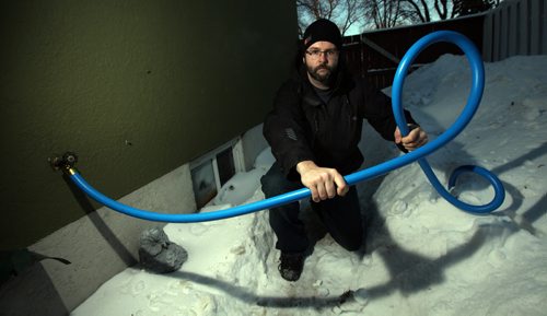 Ryan Black holds a water hose the city ran from his neighbors home after his water intake froze. See story.. February 26, 2014 - (Phil Hossack / Winnipeg Free Press)