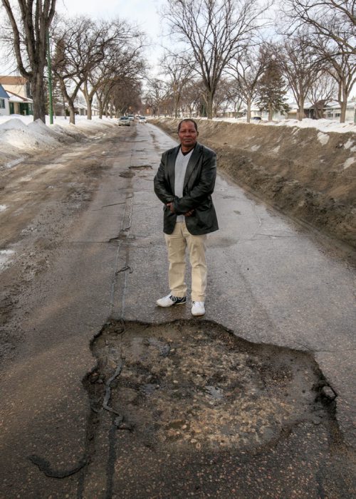 Richard Mutungi, owner of Winncity Driving School, stands in a large pothole on Inkster Blvd near Sinclair Street Thursday morning. Muntungi advises drivers to keep a safe distance, slow for potholes and don't swerve.  140313 - Thursday, {month name} 13, 2014 - (Melissa Tait / Winnipeg Free Press)