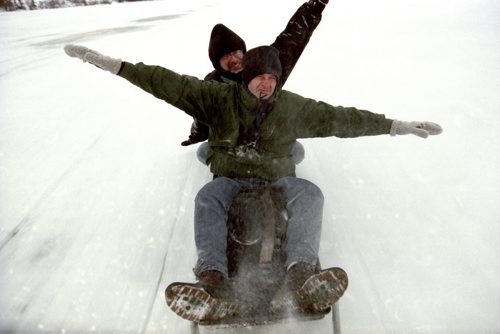 Winnipeg Free Press Photojournalist Jeff de Booy, being pulled behind a snowmobile, along with Free Press reporter Dave Supleve on assignment in St. Theresa Point, Manitoba covering an aeroplane crash. November 1993. Photo by Winnipeg Sun Photojournalist Aaron Harris.