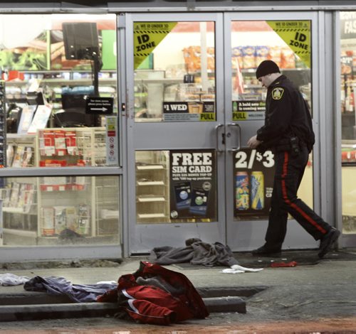 A Police officer walks past items of clothing items in the taped off parking lot of the 7 Eleven store on Main Street at Bannerman Ave. Wednesday morning after a reported stabbing incident. A section of sidewalk on Main St. just south of the store is also taped off.    Wayne Glowacki / Winnipeg Free Press March 26   2014