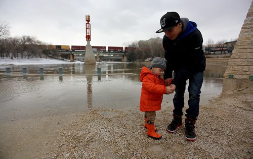 With nearby supervision, Nakoa Mastroianni, 2, and his uncle, Thomas Sinclair, 14, gather some small pebbles to throw into the Assiniboine River as they stand on the partiall submerged walking path at The Forks, Sunday, April 13, 2014. (TREVOR HAGAN/WINNIPEG FREE PRESS)