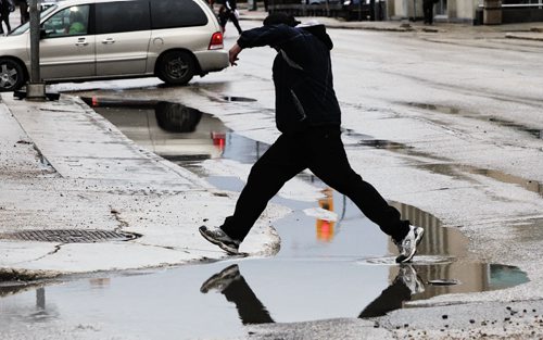 A pedestrian jumps over a water filled pothole in downtown Winnipeg Monday morning.  140428 April 28, 2014 Mike Deal / Winnipeg Free Press