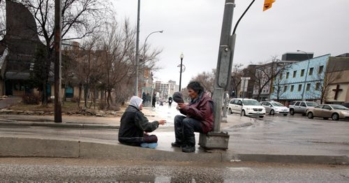 A pair of Main street's "street" people huddle on the median at Higgins and Main Monday afternoon seeking shelter from the rain and panhandling cars at the red light. April 28, 2014 - (Phil Hossack / Winnipeg Free Press)