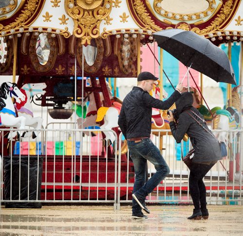 Stefan Froese shields his wife Lisa Goethals from rain as she checks out possible backgrounds for a photo shoot at a closed and wet Wonder Shows carnival near the Forks on Victoria Day. 140519 - Monday, May 19, 2014 - (Melissa Tait / Winnipeg Free Press)