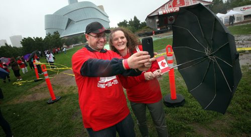 Ward Bruner and his wife Jennifer Wilson hang onto their umbrella and smart phone trying to take a selfie in the blowing rain before taking part in the formation  of a human flag formed despite the weather at the Forks Tuesday.  See Oliver's story. July 1, 2014 - (Phil Hossack / Winnipeg Free Press)