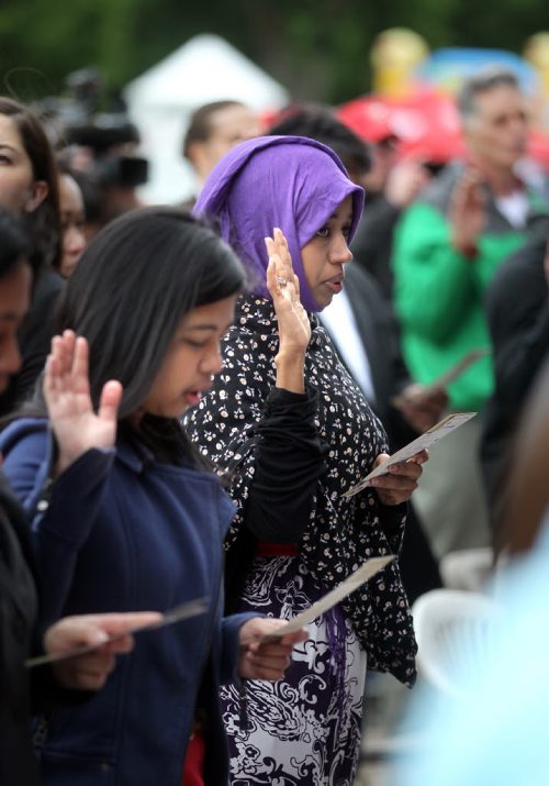 New citizens raise their right hands and recite the Oath of Citizenship Tuesday at a ceremony held at the Lyric Stage in Assinaboine park Tuesday.  See story. July 1, 2014 - (Phil Hossack / Winnipeg Free Press)