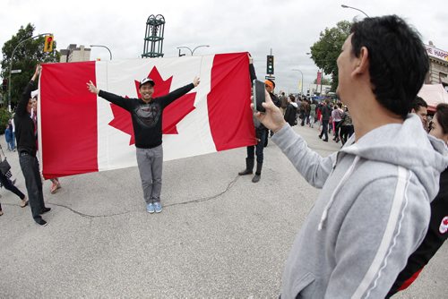 July 1, 2014 - 140701  -  Junjun Dalisay poses for a photo by his friend Jorge Sy against a large flag in Osborne Village in Winnipeg Tuesday, July 1, 2014.. Cousins Henry and Langley Duck walked with a large Canada throughout Winnipeg and encouraged people to take their photo against it during Canada Day celebrations.   John Woods / Winnipeg Free Press