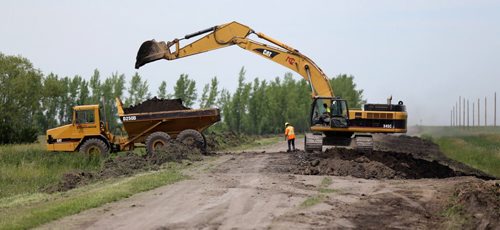 Construction crews work to bulk up the east side of the Portage Diversion near Highway 1, Saturday, July 5, 2014. They are removing dirt from along the road and dumping it on the bank.  (TREVOR HAGAN/WINNIPEG FREE PRESS)