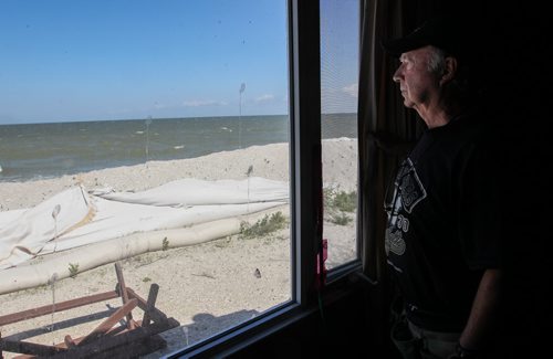 Frank Renouf looks out the window of his niece's cottage that is protected by a tube dike that runs along the beach at Twin Lakes Beach. Some of the tubes have been damaged by ice from last winter and his family is concerned that they won't hold in the coming weeks. 140706 - Sunday, July 06, 2014 -  (MIKE DEAL / WINNIPEG FREE PRESS)
