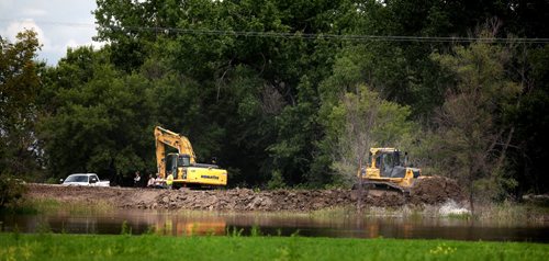 Earth movers and trucks fill in a gap on the Assinaboine River Dike near St Eustashe. See story. July 8, 2014 - (Phil Hossack / Winnipeg Free Press)