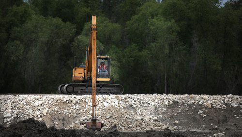 A heavy equipment operatormoves rip-rap to reinforce a section on the Assinaboine River Dike between St Eustashe and Portage la Prairie. See story. July 8, 2014 - (Phil Hossack / Winnipeg Free Press)