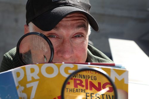 Winnipeg Fringe Festival Executive Producer --  Chuck McEwen hams it up for the camera as he examines this year's program (We like it when you Watch) at the Festival's MainStage in Old Market Square.   July 15, 2014 Ruth Bonneville / Winnipeg Free Press