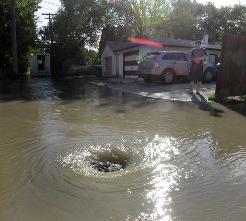 Chris Johnson watches water drain into a backlane sewer behind is home on Kylemore Ave. after a water main break Wednesday morning flooded nearby streets in the Lord Roberts neighbourhood. Wayne Glowacki / Winnipeg Free Press July 23  2014