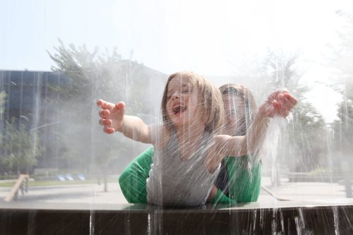 Five year old Sophie Bollman reaches out to touch the streams of water pouring down from the "empty full" water feature in the Millennium Library Park Tuesday morning while her mom holds her up to reach it.  Marnie Bollman and her daughter were making the most of their extra time downtown before it was time to pick up Sophie's little brother from daycare. Standup photo  July 29, 2014 Ruth Bonneville / Winnipeg Free Press