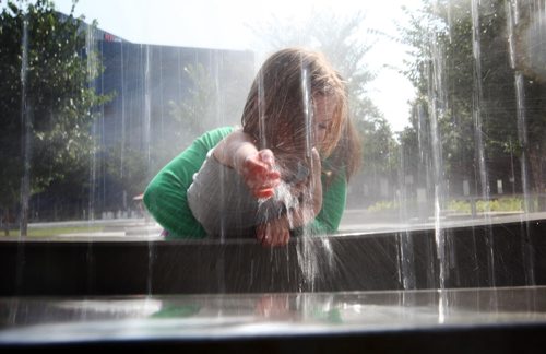 Five year old Sophie Bollman reaches out to touch the streams of water pouring down from the "empty full" water feature in the Millennium Library Park Tuesday morning while her mom holds her up to reach it.  Marnie Bollman and her daughter were making the most of their extra time downtown before it was time to pick up Sophie's little brother from daycare. Standup photo  July 29, 2014 Ruth Bonneville / Winnipeg Free Press
