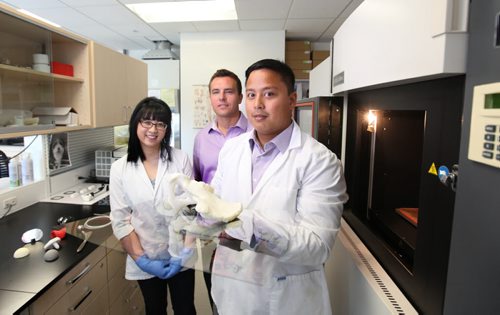 Orthopaedic Innovation Centre Director, Dale Kellington (centre, purple shirt),  Leah Guenther - Manager of Biomedical Engineering and Lawrence Cruz - Lab Technologist, stand next to a 3D printer, also known as a  Fused Deposition Modeling (or FDM) machine which looks like a large oven. It heats up and quickly cools a polycarbonate material and using precision technology creates  bone-like tissues that can be used for modelling purposes or hip and knee components in the human body.  Lawrence Cruz holds a half pelvic model developed from a CT scan and printed in this 3D printer in their facility for the purpose of surgical planning. The company also has a patent for infusing antibiotics into these components before they are surgically implanted into the human body.  See story Cash story.    July 30, 2014 Ruth Bonneville / Winnipeg Free Press