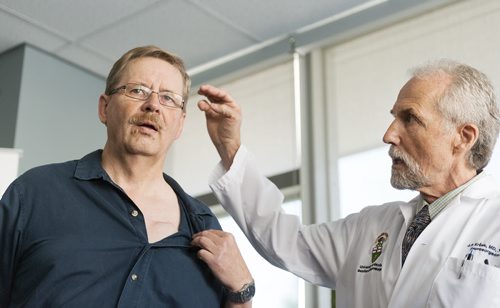 HSC neurosurgeon Dr. Jerry Krcek (right) shows where the micro-electrode is in Doug Martens' brain and the pace maker it is connected to in his chest. Martens was diagnosed with Parkinson's in 2003 and underwent deep brain stimulation surgery in early 2014 and says his quality of life has greatly improved.  Sarah Taylor / Winnipeg Free Press August 12, 2014