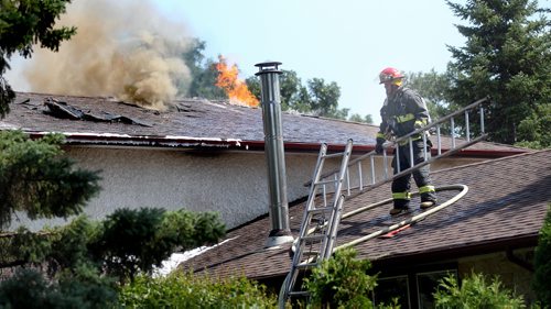 A firefighter pulls equipment aff the roof at 54 Nichols ave Friday afternoon as crews were evacated to a defensive position outside two homes as they were destroyed by fire. Crews battled the fire as well as extreme heat. See story. August 15, 2014 - (Phil Hossack / Winnipeg Free Press)