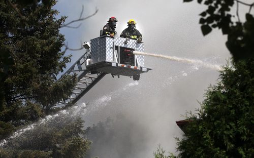 Framed in suburban foliage, Firefighters man an arial unit fighting a blaze that started at 54  Nichols ave Friday afternoon, two homes went up in flames. Crews battled the fire as well as extreme heat. See story. August 15, 2014 - (Phil Hossack / Winnipeg Free Press)