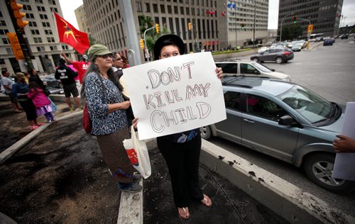 Protestors, many of them women and children stand on all four corners of Portage and Main street Friday afternoon during rush hour. Holding placcards protesting the Harper Governments decision not to hold an enquiry into the missing and murdered women. See release/story. August 22, 2014 - (Phil Hossack / Winnipeg Free Press)