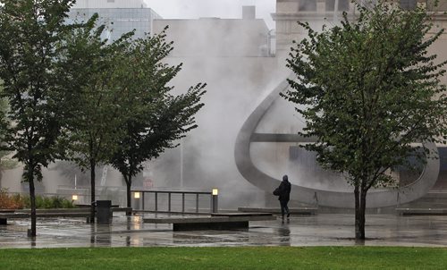 A pedestrian walks through the heavy mist that is being created by the "Emptyful" sculpture in the Millennium Library Plaza Sunday morning.  140824 August 24, 2014 Mike Deal / Winnipeg Free Press
