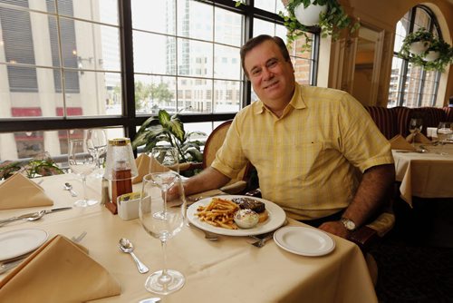 THIS CITY - Bailey's Restaurant & Lounge with  Leo Groumoutis (owner)in the Winter Garden Room  : This is for a Sunday This City profile of Bailey's - a downtown institution since the early 70s. Owner Leo Groumoutis started there as a 13-year-old dishwasher and, a couple of decades later, ended up buying the place together with his brother George.  So shots of Leo - maybe holding up one of Bailey's signature dishes (they make a killer steak sandwich) - in one of the restaurant's dining rooms. We'll have room for five or six pics so also shots of the exterior - the lounge & pool table area, the library room - and if possible, there are a series of hidden tunnels in the basement that lead throughout the downtown - Leo used to play hide and seek down there as a kid, so that might be an interesting pic, too....story by Dave Sanderson .Aug 26 2014 / KEN GIGLIOTTI / WINNIPEG FREE PRESS