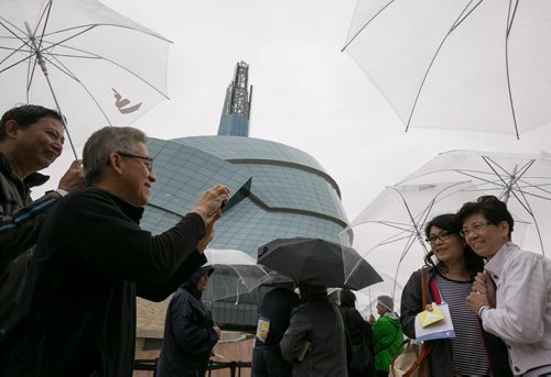 Frank Yong snaps a photo of his wife Teresa and her friend Jenny Lee, all from BC, while they wait in the rain for their preview tour at the Canadian Museum for Human Rights on Saturday. The rain kept away some of the people with reserved tickets, allowing walk-ups to gain access to the guided tour of four of 11 galleries. The rest of galleries open September 27th. 140920 - Saturday, September 20, 2014 - (Melissa Tait / Winnipeg Free Press)