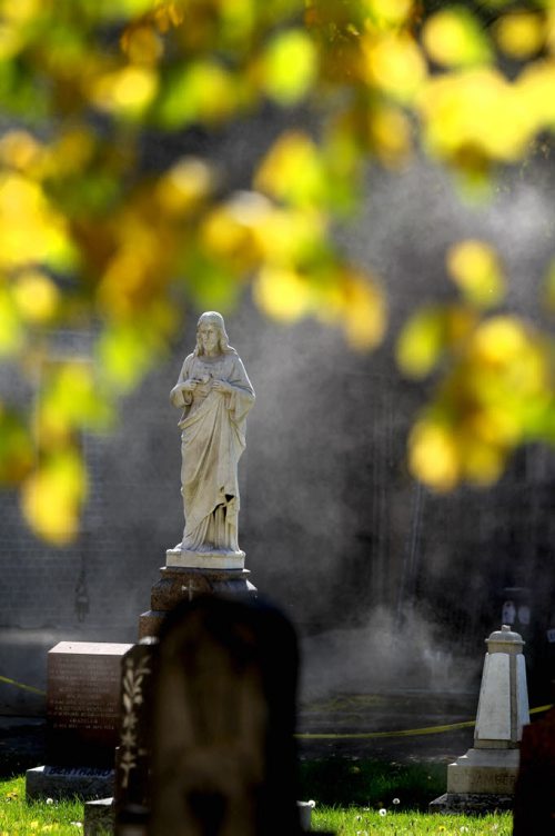 Autumn leaves glow as they drape from the branches of a large tree like a canopy over the tombstones and statues in the cemetery outside the St. Boniface Basilica and the Grey Nuns Thursday afternoon in the warm sunshine.   Standup photo.  Sept 25,  2014 Ruth Bonneville / Winnipeg Free Press