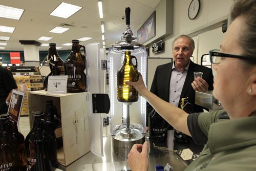 At the official launch Friday of the pilot program of in-store Growler Bars at five Liquor Mart and two beer vendor locations in Winnipeg and Brandon, Ron Lemieux, Minister responsible for Manitoba Liquor & Lotteries watches Tracy Jones a Liquor Mart customer service rep. place a Growler bottle in the filling equipment at the Kenaston Crossing Liquor Mart. The 1.89 litre refillable Growler you purchase is filled by a Liquor Mart staff person with a craft beer.   see release. Wayne Glowacki/Winnipeg Free Press Oct.24  2014