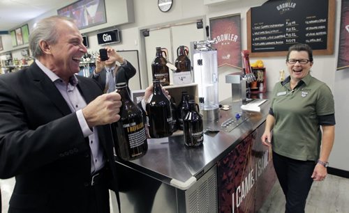 At the official launch Friday of the pilot program of in-store Growler Bars at five Liquor Mart and two beer vendor locations in Winnipeg and Brandon, Ron Lemieux, Minister responsible for Manitoba Liquor & Lotteries grabs two Growler bottles for Tracy Jones a Liquor Mart customer service rep. to fill at the Kenaston Crossing Liquor Mart. The 1.89 litre refillable Growler you purchase is filled by a Liquor Mart staff person with a craft beer.   see release. Wayne Glowacki/Winnipeg Free Press Oct.24  2014
