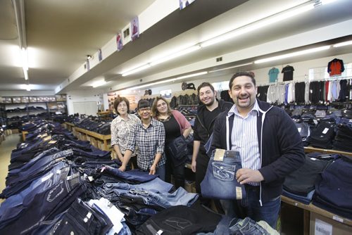 Sargent Blue Jeans located at 1136 Sargent Ave.  Mohamed El tassi (right, front) one of the owners of Sargent Blue Jeans, poses with some of the longtime staff at the neighbourhood Jean store between long tables of high-end designer jeans,  Names - Mohamed El tassi (right), Mohamed Tassi (black hoodie), Sandra Harold (plaid shirt), Maria Lima (pink sweater) and Kathy Malandrakis (last in row).  David Sanders feature story.   Oct 30,  2014 Ruth Bonneville / Winnipeg Free Press