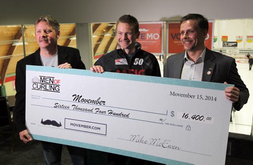 STANDUP - Curling champ Mike McEwen is centred by Movember Winnipeg Co-Chairs Jeff Palson, right,  Jamie Hopkins, left. McEwen presented Movember Winnipeg's organizing committee with a donation of $16,400, raised from the 2014 Men of Curling calendar that the curling superstar was part of this past year. Photo taken at Fort Rouge Curling Club  750 Daly Street. BORIS MINKEVICH / WINNIPEG FREE PRESS November 17, 2014