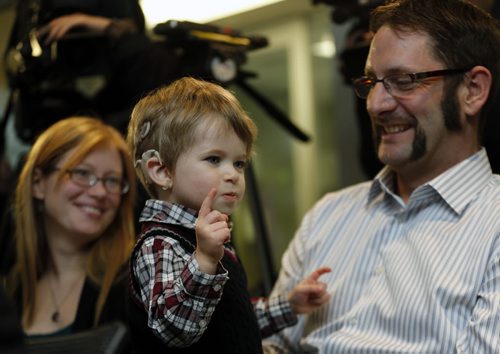 LOCAL - LtoR mother Erin Spears with  Mathew Spears age 2 wearing Cochlear implants talks with his dad Ian at newser .Hearing Surgery Program Reaches Milestone 100 Manitobans receive Cochlear Implant device, patients hear things they never heard before WHAT: The surgical hearing implant program at Health Sciences Centre Winnipeg, in partnership with Central Speech and Hearing Clinic, offers a local choice for Manitobans to receive all aspects of care including preoperative evaluation, surgery and post-operative rehabilitation. The three-year-old program recently performed the 100th surgery to insert a cochlear hearing device. A cochlear implant is a small electronic device that can help to provide a sense of sound by electrical stimulation of the auditory nerve to a person who is profoundly deaf or severely hard-of-hearing. Adults who have lost all or most of their hearing later in life can benefit from cochlear implants by associating the sounds made through an implant with sounds they remember. Cochlear implants, together with intensive post-implant auditory-verbal therapy, help young children learn to use their device to develop speech . Story by kevin rollason NOV. 17 2014 / KEN GIGLIOTTI / WINNIPEG FREE PRESS