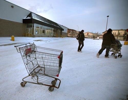 Area residents walk past an abandoned shopping cart in the empty parking lot of an abandoned "Extra Foods" on Notre Dame. Residents in two older Winnipeg neighbourhoods are getting back something they lost two years ago -- a discount grocery store for their area. Loblaws has confirmed it will be converting its former Extra Foods stores on Notre Dame and Main Steet  into No Frills grocery stores. Both new franchises to open sometime in the first half of 2015. (McNeill. 12 Ours alone) December 2, 2014 - (Phil Hossack / Winnipeg Free Press)